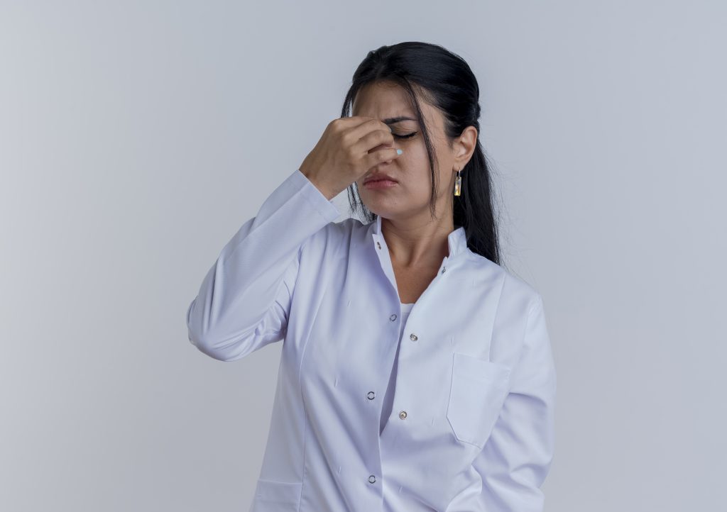 tired-young-female-doctor-wearing-medical-robe-holding-nose-with-closed-eyes-isolated-white-wall-with-copy-space