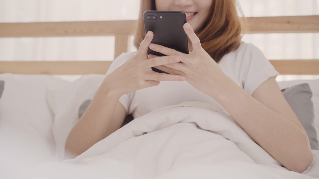 young-asian-woman-using-smartphone-while-lying-bed-after-wake-up-morning