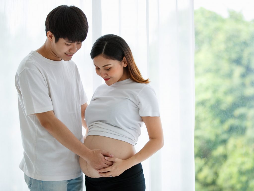 lovely-young-asian-couple-husband-wife-standing-together-smiling-touching-pregnant-woman-s-belly-with-love-care-happy-healthy-family-concept-min